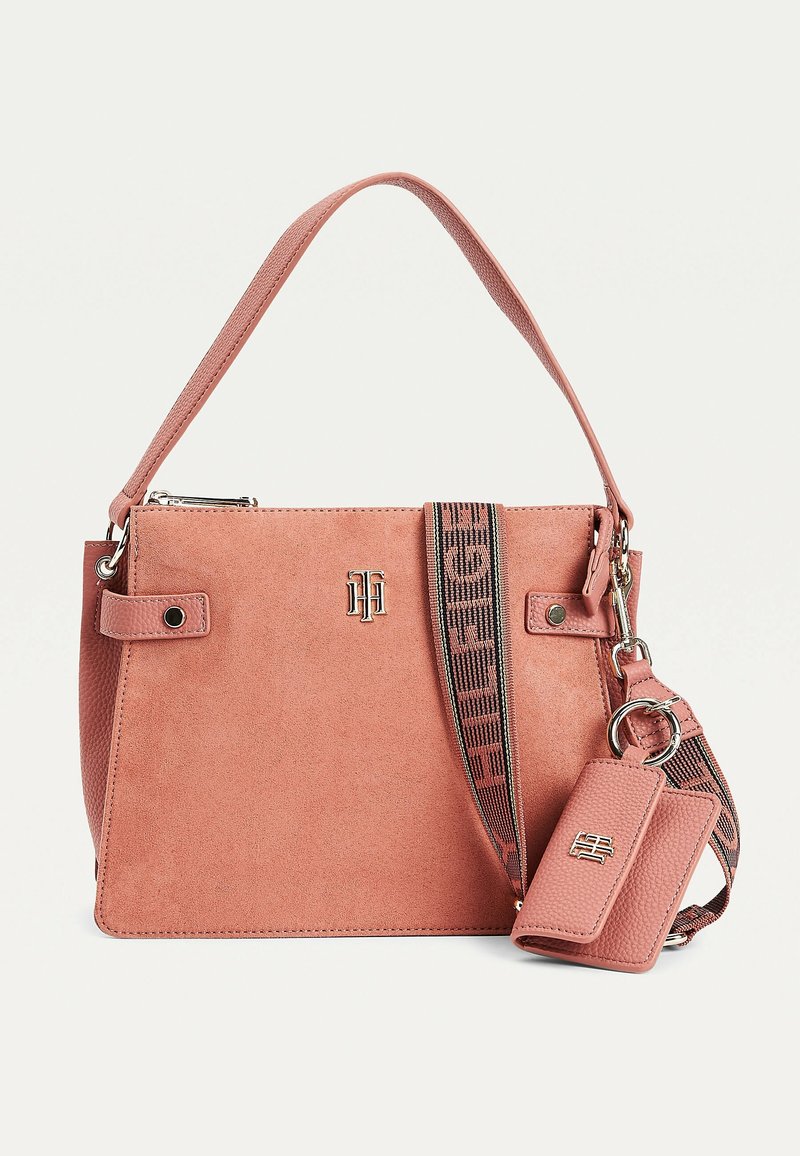 Sac à main rectangulaire en daim rose poudré avec une poignée courte, une bandoulière en tissu de marque amovible et une pochette à clés texturée assortie attachée.