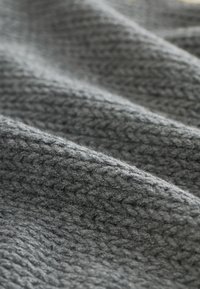 Detailný záber textúrovaného sivého pleteného materiálu s mäkkými záhybmi a jemným osvetlením zvýrazňujúcim tkaný vzor.