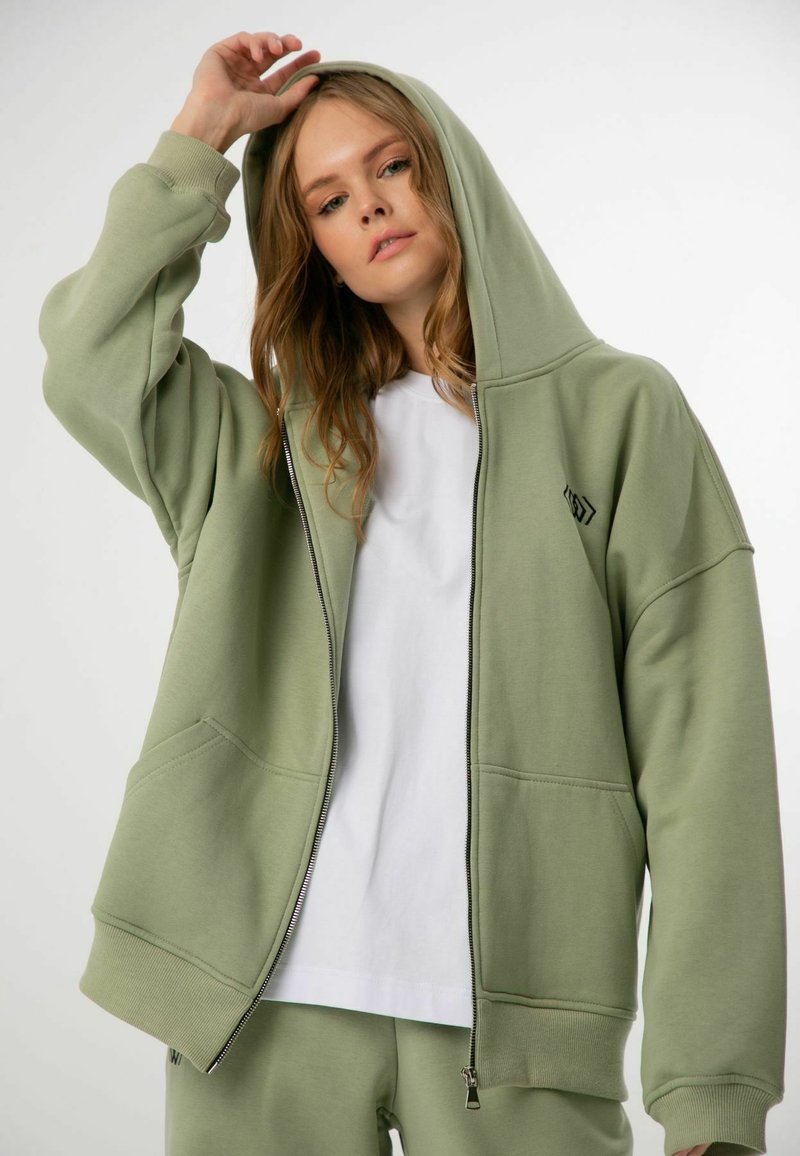 Ljusgrön zip-up hoodie med stor huva, framfickor, ribbade ärmmuddar och en liten svart logotyp på bröstet. Mjuk bomullsblandning.