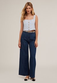 Ljusblå kort topp med fyrkantig halsringning och knappar fram, tillsammans med högmidjade mörkblå vida jeans och svartvita flats.