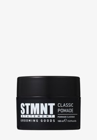 Pot de pommade rond noir avec une finition mate. Du texte blanc affiche le nom de la marque "STMT" et le type de produit "CLASSIC POMADE." Taille de 100 ml.