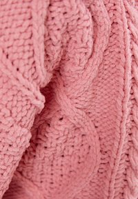 Tejido de punto texturizado en color rosa con un patrón de cable elevado, que muestra suavidad y volumen. El diseño presenta hilos intrincados e entrelazados.
