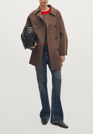 Bruin wollen mix dubbelzijdig jasje met grote kraag, gecombineerd met flared donkere denim jeans en een zwarte leren handtas. Rood shirt eronder.