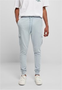 Lys blå bukser med lommer på siden, elastisk midjebånd og mansjetter, laget av mykt stoff. Bært med hvite joggesko og en uformell t-skjorte.