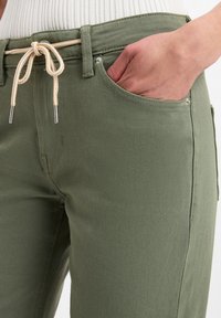 Pantaloni in misto cotone verdi con vestibilità rilassata, vita con cordoncino elasticizzato e tasche laterali con dettagli in metallo argentato.