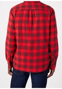 Chemise en flanelle à carreaux rouges et noirs, à manches longues, avec des poignets à boutons, un empiècement dans le dos et un ourlet arrondi. Texture douce sur toute la surface.