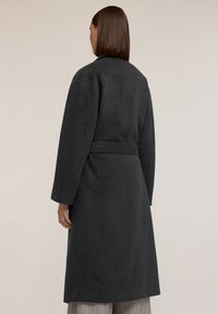 Abrigo largo de color gris oscuro con cinturón, con mangas amplias y una silueta simple. Textura de tela suave, diseño minimalista sin patrones.