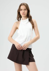 Witte mouwloze top met hoge hals, gecombineerd met een bruin wikkel minirokje. Soepele stof met een aansluitende pasvorm en een minimalistisch ontwerp.