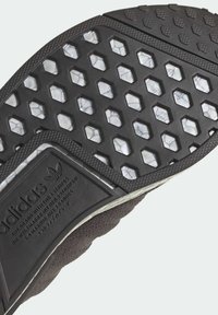 Närbild av Adidas-skoens sula med hexagonal mönster och varumärkestext präglad på den svarta gummihäl.