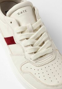 Sneaker bianca in pelle con una striscia rossa accentuata, lacci piatti colore crema, punta perforata e logo in rilievo sulla linguetta.