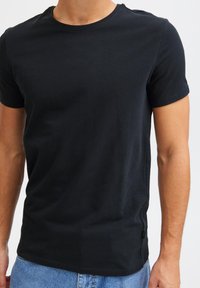 Maglietta nera in cotone con scollo rotondo, maniche corte e spacco laterale. Tessuto morbido con cuciture minimali e piccola etichetta logo sull'orlo.