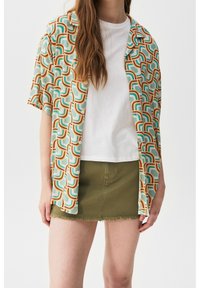 Short-sleeve shirt with a mint green base featuring a geometric pattern in orange and blue, paired with a white t-shirt and olive green skirt.