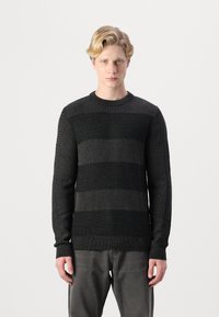 Maglione a strisce nere con motivo a maglia testurizzato. Maniche lunghe e polsini a coste. Indossato con pantaloni grigi. Design semplice e aderente.