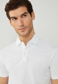 Polo bianco realizzato in cotone morbido, con colletto, patta con tre bottoni e un piccolo logo ricamato sul petto.