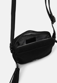 Czarna torebka na ramię z teksturowaną powierzchnią, zamkiem błyskawicznym i regulowanym paskiem. W środku znajduje się kieszeń z drukowaną podszewką. Zawiera akcent w postaci frędzla.