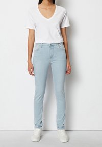 Jeans ajustados de color azul claro de denim, combinados con una camiseta básica de cuello en V blanca y zapatillas blancas. Se ajustan estrechamente al cuerpo.