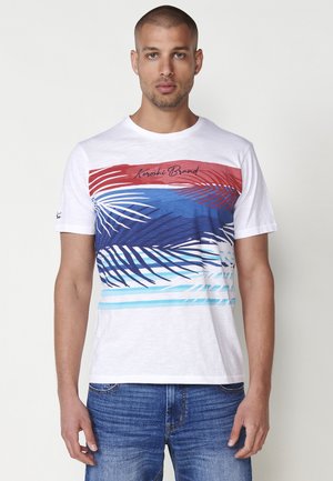 Witte T-shirt met een kleurrijk palmbladontwerp in rood, blauw en turquoise, met "Karoshi Brand" gedrukt over de borst.
