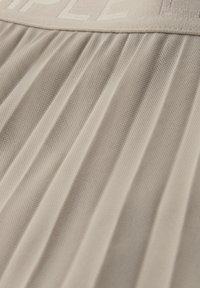 Beige geplooide stof met een getextureerde tailleband met verhoogde, deels zichtbare tekst of patroon.