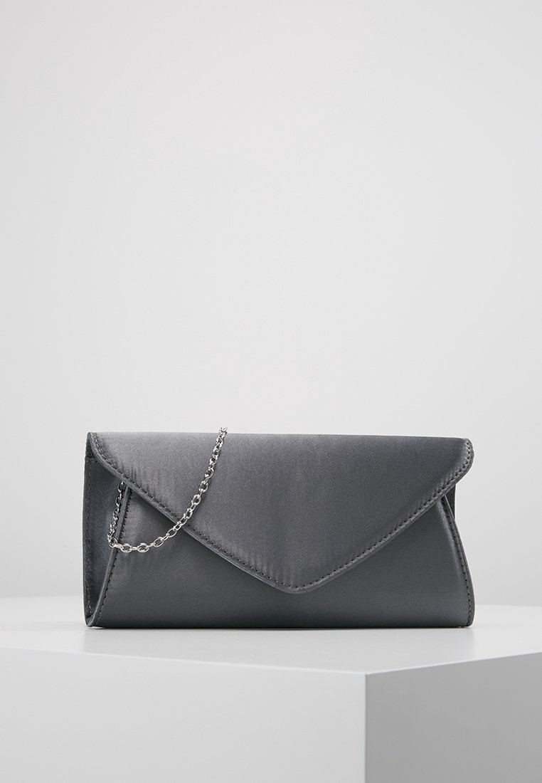Pochette enveloppe en satin gris avec bandoulière chaîne argentée reposant sur une surface blanche sur un fond gris uni.