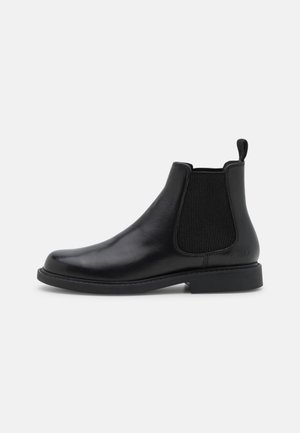 Bota Chelsea de cuero negro con paneles laterales elásticos, tira para tirar en la parte trasera y tacón bajo apilado, vista lateral.