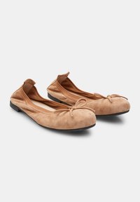 Suede ballet flats in light beige with a rounded toe and bow detail at the front, featuring a flat, black rubber sole.