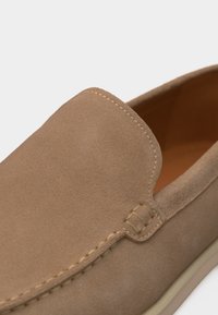 Καφέ σουέτ μοκασίνι με ορατή ραφή και επένδυση με επένδυση, εμφανιζόμενο σε κοντινή προβολή.