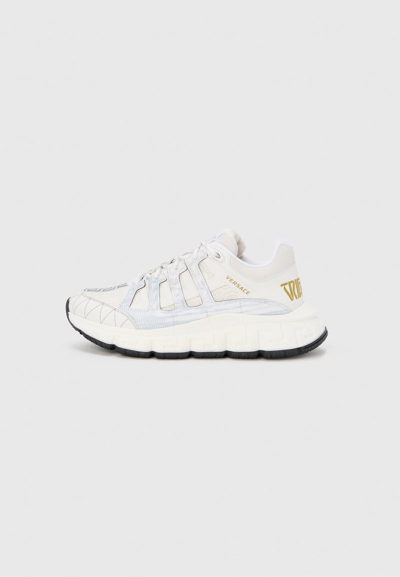 White sneakers with a textured pattern, featuring a thick, cushioned sole, black detailing, and gold branding on the side.