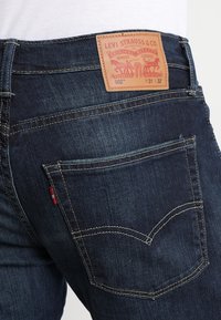 Jeans de mezclilla oscura con una etiqueta de cuero, que incluyen bolsillos traseros, costuras en contraste y el logo de Levi Strauss grabado en la etiqueta.