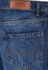 Siniset farkut, joissa on takatasku oranssilla ompeleella ja ruskea nahkainen etiketti, jossa lukee "URBAN CLASSICS DENIM FACTORY."