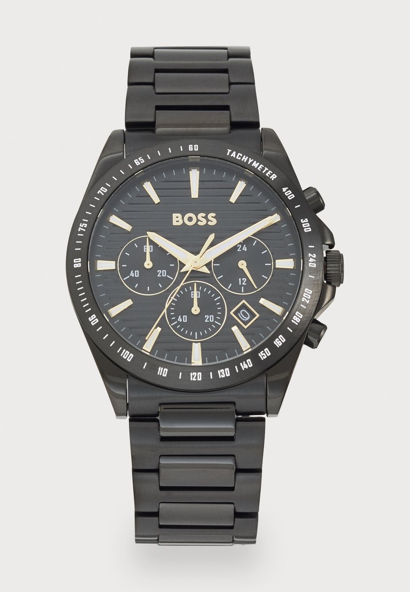 Montre en métal noir avec un cadran noir texturé, des accents dorés et trois sous-cadrans. Présente un bracelet en acier inoxydable et des repères de tachymètre.