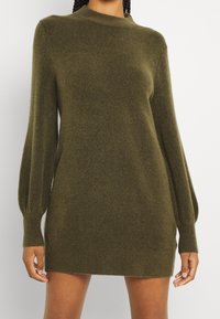 Abito maglione verde oliva realizzato in morbido tessuto a maglia, con collo alto e maniche a palloncino. Lunghezza corta con polsini e orlo a coste.