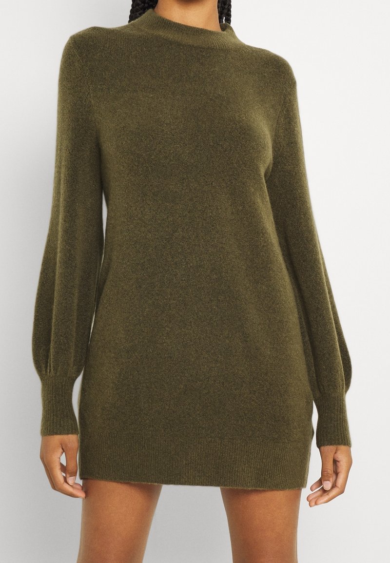 Abito maglione verde oliva realizzato in morbido tessuto a maglia, con collo alto e maniche a palloncino. Lunghezza corta con polsini e orlo a coste.