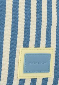Sac en tissu rayé de couleurs bleu et crème, avec un motif texturé. Inclut une étiquette en cuir bleu portant la mention "TOM TAILOR" en relief.