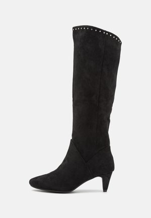 Czarny zamszowy kozak sięgający do kolan z zaostrzonym noskiem i obcasem o średniej wysokości. Ozdobiony dekoracyjnymi srebrnymi ćwiekami wzdłuż górnej krawędzi. Gładka faktura.