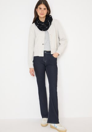 Cardigan gris clair sur un haut gris, associé à un jean pattes d'eph bleu foncé. Écharpe noire avec des accents blancs. Baskets crème avec des détails bleus.