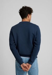 Sudadera azul marino con cuello redondo y puños de canalé, confeccionada en una tela suave, exhibida desde la parte posterior con las manos entrelazadas.