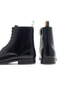 Czarne skórzane botki za kostkę mają gładkie wykończenie, sznurowany fason oraz kontrastową pętlę z zielonymi, białymi i czerwonymi paskami.