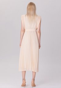 Robe midi plissée en tissu pêche doux avec une taille cintrée et de douces volants aux épaules. Présente une silhouette fluide et une texture délicate.
