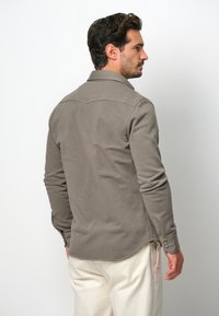 Camicia in cotone grigia con colletto, maniche lunghe, orlo curvo e polsini abbottonati. Texture liscia senza motivi o loghi visibili.
