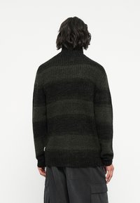 Strickpullover in dunkelgrün und schwarzen Streifen, mit hohem Kragen und gerippten Bündchen. Strukturierter Stoff mit lockerer Passform.