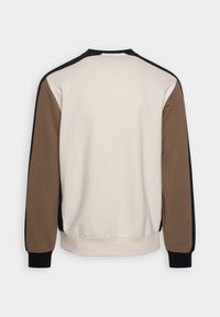 Sweatshirt met een crèmekleurige achterkant, bruine lange mouwen, zwarte accenten op de schouders en manchetten, getoond van achteren tegen een witte achtergrond.