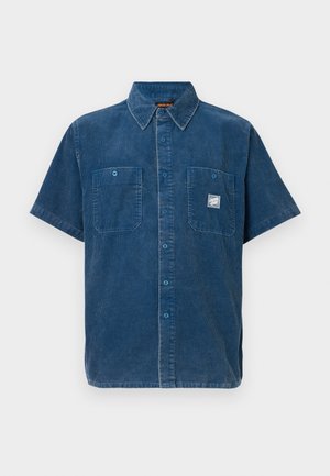 Modrá košeľa z manšestru s krátkym rukávom a zapínaním na gombíky, s dvoma náprsnými vreckami, z ktorých jedno má malú bielu logo nášivku.