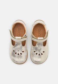 Zapatos infantiles de cuero plateado con purpurina, puntera cerrada, diseño de flor recortado, correa ajustable y plantilla de cuero marrón.