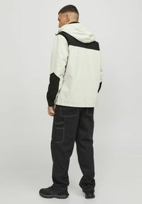 Giacca con cappuccio bianca e nera con un design a contrasto, abbinata a pantaloni cargo neri con più tasche e cuciture bianche.