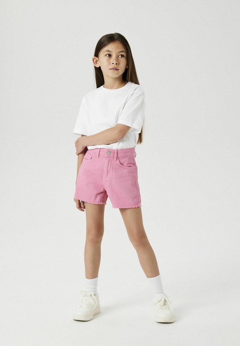 Shorts en denim roses avec une taille haute et un ourlet effiloché, associés à un t-shirt en coton blanc et des baskets blanches. Design simple et ajustement confortable.