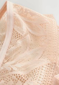 Blondebralette i blid lyserød med indviklede blomsterdesignet, en tekstureret overflade og en delikat elastikbånd langs kanterne.