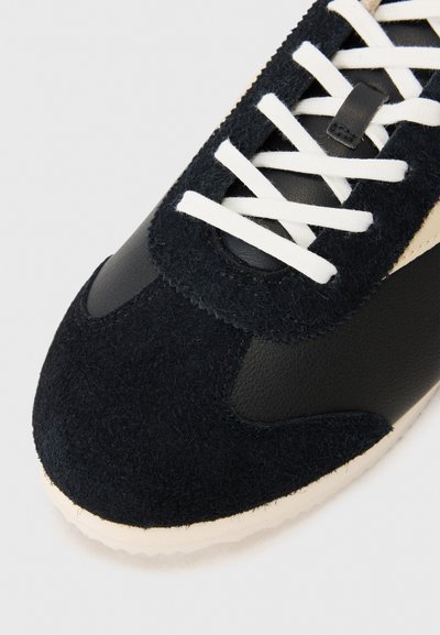 Black athletic shoe featuring a combination of suede and leather, with white laces, rounded toe, and a textured outsole for traction.