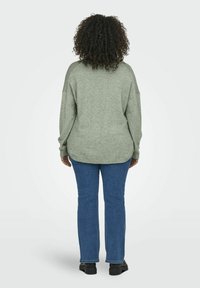 Svetle zelený oversized svetr s kleslými rameny, strukturovanou tkaninou, žebrovaným lemem, který je zkombinován s modrými rovnými džíny a černými botami.