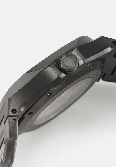 Schwarze Edelstahl-Uhr mit matter Oberfläche, achteckiger Krone, strukturierten Gehäusekanten und glatten Armbandgliedern. Sichtbare Details auf dem Gehäuseboden.