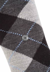 Calzini argyle grigi con accenti neri, grigi chiari e blu. Presentano un logo metallico rotondo al centro. Realizzati in materiale lavorato a maglia.